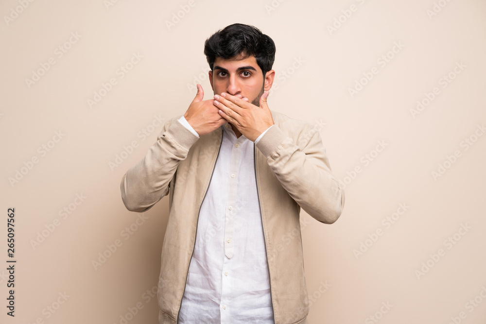 Young man over isolated wall covering mouth with hands Young man over isolated wall covering mouth with hands