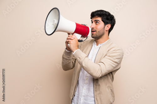 Young man over isolated wall shouting through a megaphone