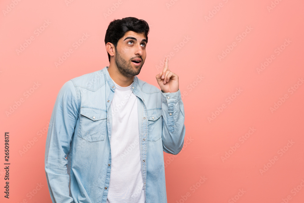 Young man over pink wall thinking an idea pointing the finger up Young man over pink wall thinking an idea pointing the finger up