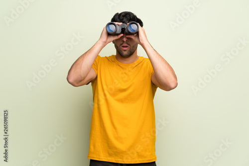 Young man over pink wall and looking in the distance with binoculars