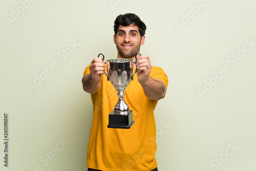 Young man over pink wall holding a trophy