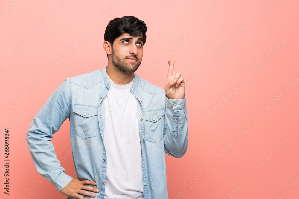 Young man over pink wall with fingers crossing and wishing the best Young man over pink wall with fingers crossing and wishing the best