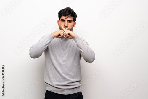 Young man over isolated white wall showing a sign of silence gesture