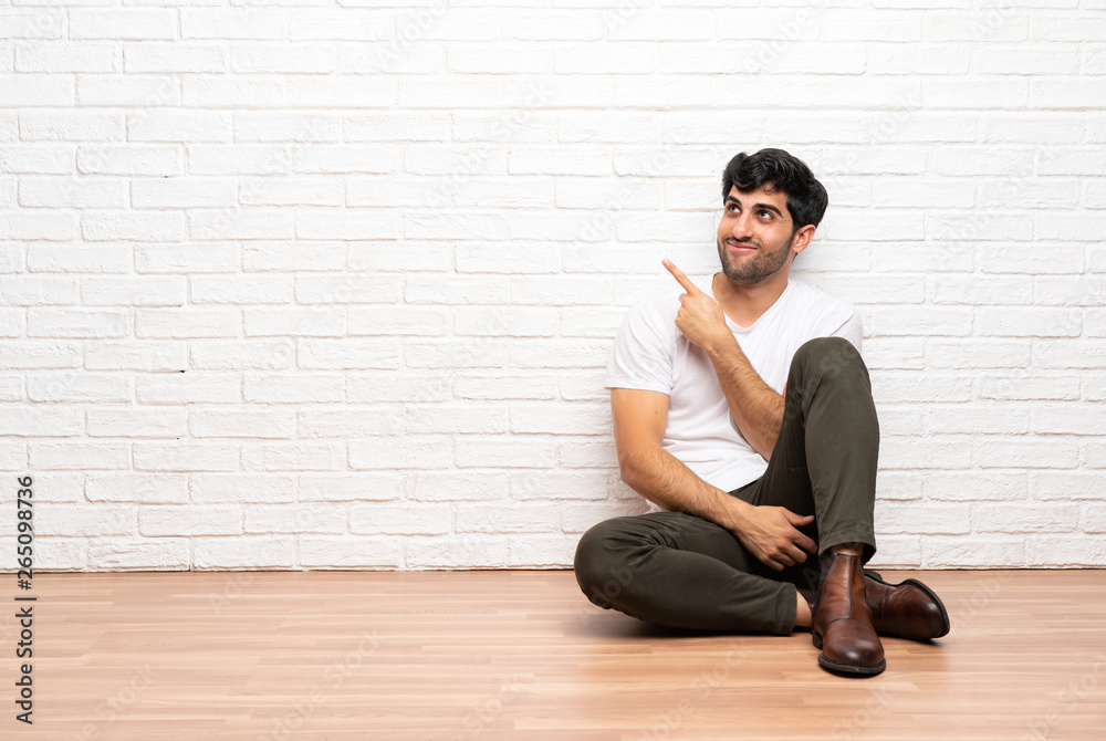 Young man sitting on the floor pointing finger to the side
