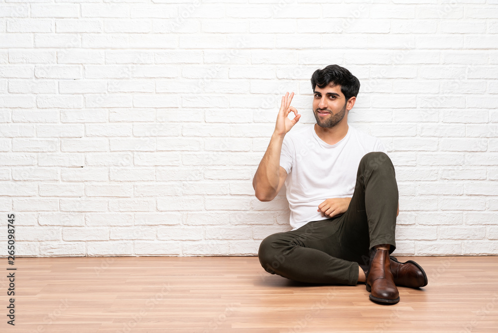 Young man sitting on the floor showing ok sign with fingers Young man sitting on the floor showing ok sign with fingers