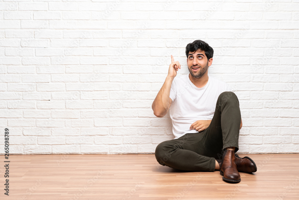 Young man sitting on the floor intending to realizes the solution while lifting a finger up Young man sitting on the floor intending to realizes the solution while lifting a finger up
