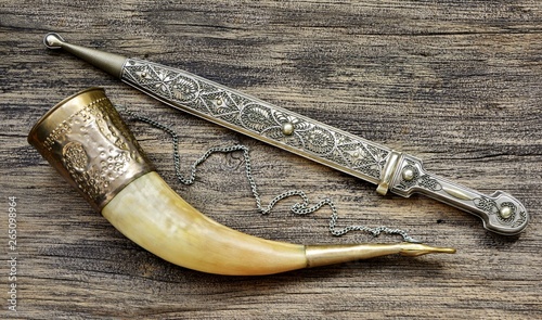 Konstfotografi Caucasian dagger and wine horn on wooden background close-up