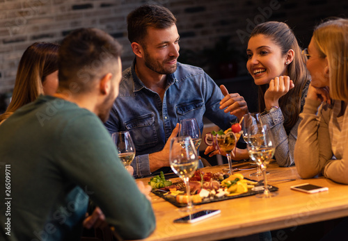 Group of young friends having fun in restaurant, talking and laughing while dining at table.