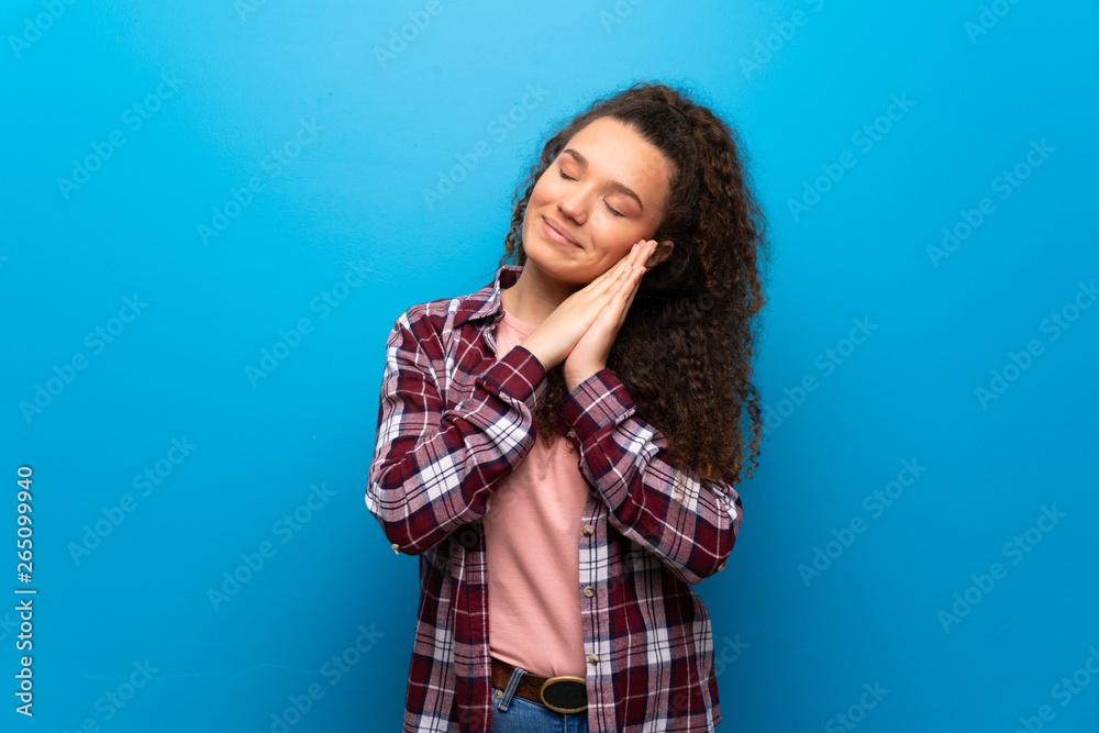 Teenager girl over blue wall making sleep gesture in dorable expression Teenager girl over blue wall making sleep gesture in dorable expression