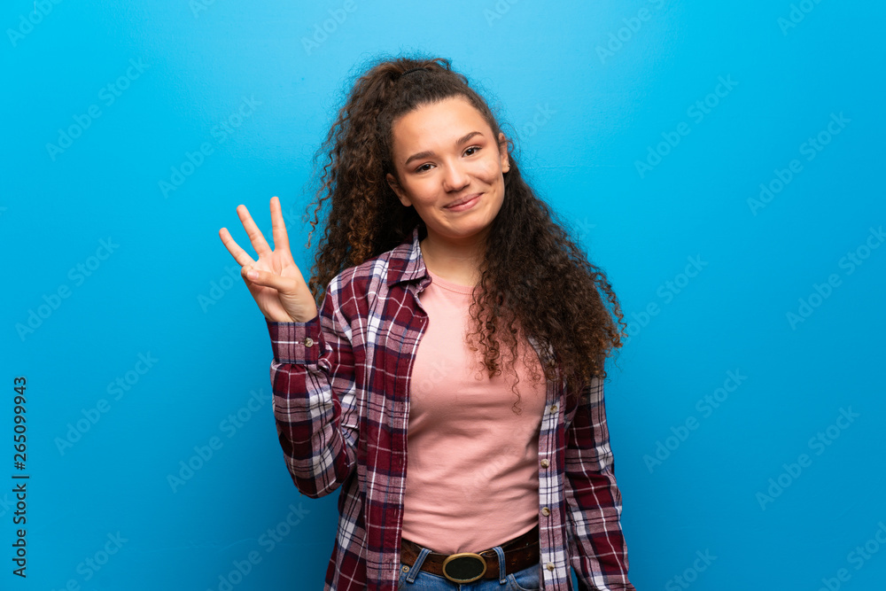 Teenager girl over blue wall happy and counting three with fingers Teenager girl over blue wall happy and counting three with fingers