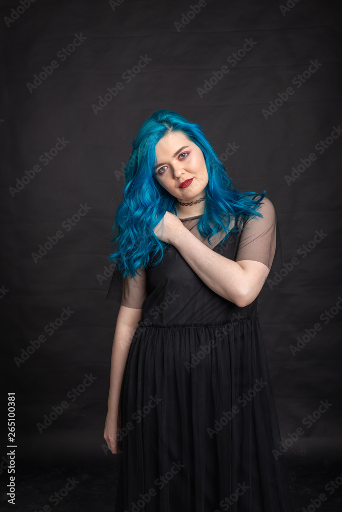 People and fashion concept - Woman with blue long hair dressed in black dress posing over black background
