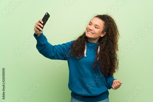 Teenager girl over green wall making a selfie