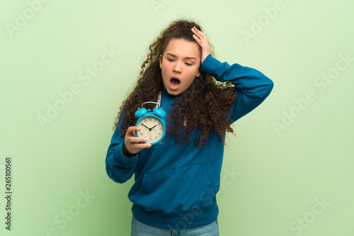 Teenager girl over green wall restless because it has become late and holding vintage alarm clock © luismolinero