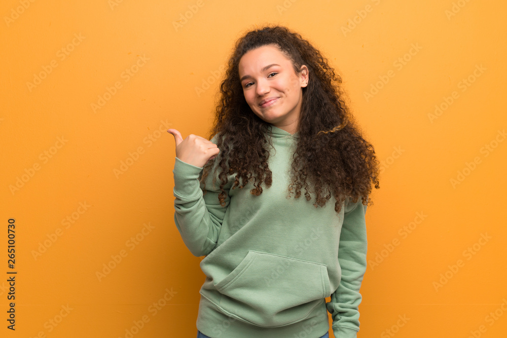 Teenager girl over ocher wall pointing to the side to present a product Teenager girl over ocher wall pointing to the side to present a product