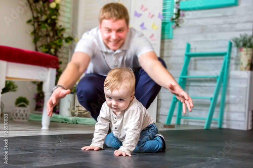 A happy father playing with son. He is trying to catch a happy child crawling on all fours.