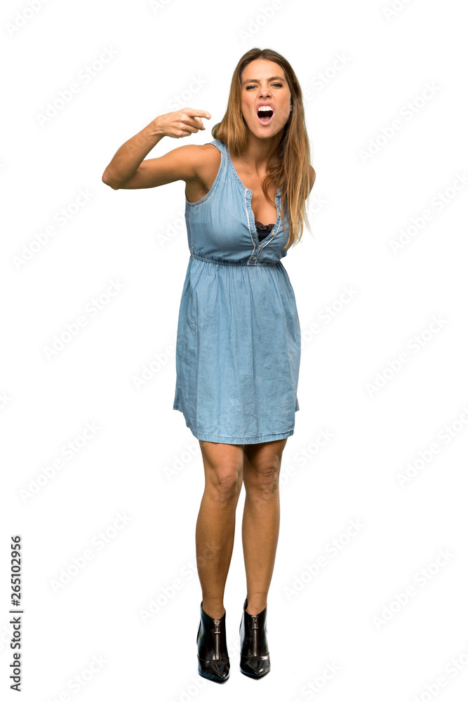 A full-length shot of a Blonde woman with jean dress frustrated and pointing to the front over isolated white background A full-length shot of a Blonde woman with jean dress frustrated and pointing to the front over isolated white background