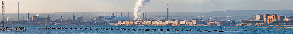 Panoramic view of Taranto, Puglia, Italy, old town with steel plant, cover of mining parks and petrochemical industry immediately behind, sunset on the sea