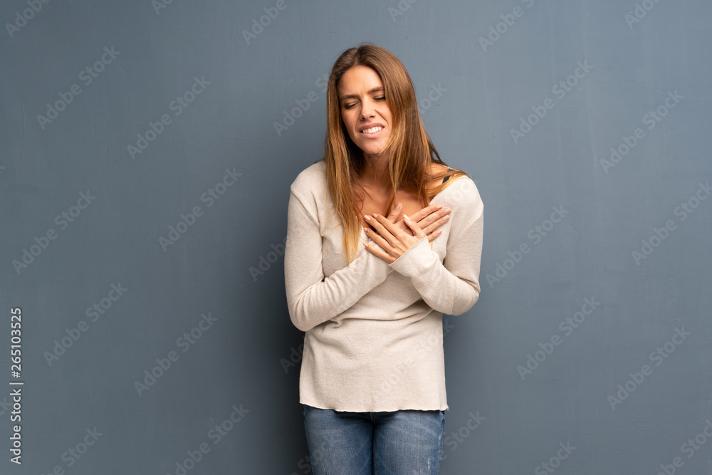 Blonde woman over grey background having a pain in the heart Blonde woman over grey background having a pain in the heart