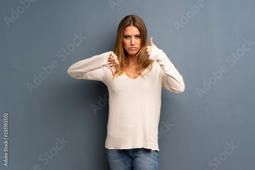 Blonde woman over grey background making good-bad sign. Undecided between yes or not