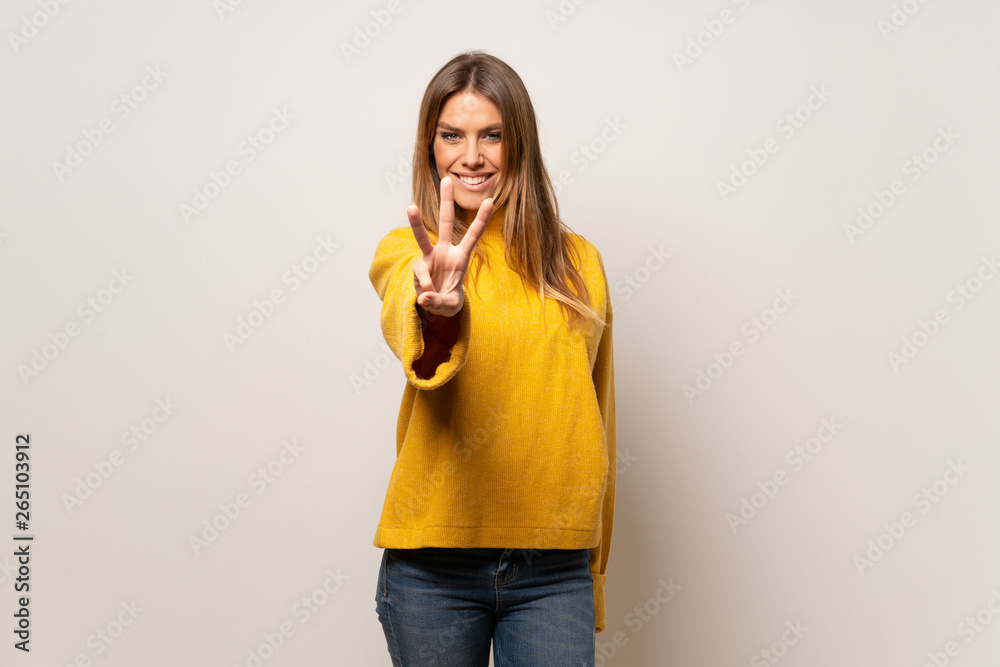 Woman with yellow sweater over isolated wall happy and counting three with fingers Woman with yellow sweater over isolated wall happy and counting three with fingers