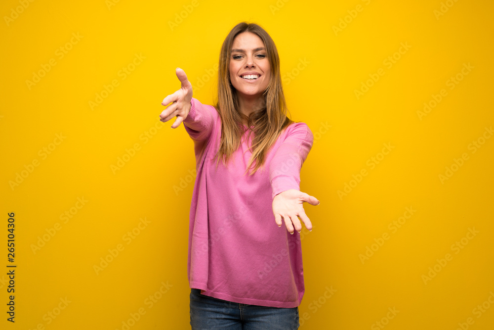 Woman with pink sweater over yellow wall presenting and inviting to come with hand Woman with pink sweater over yellow wall presenting and inviting to come with hand