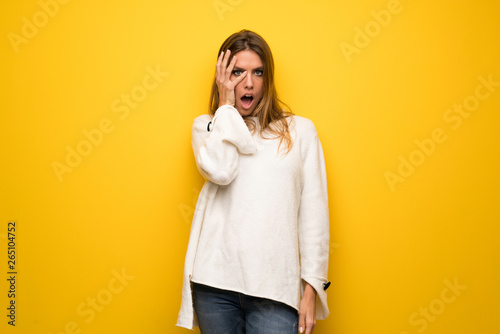 Blonde woman over yellow wall with surprise and shocked facial expression