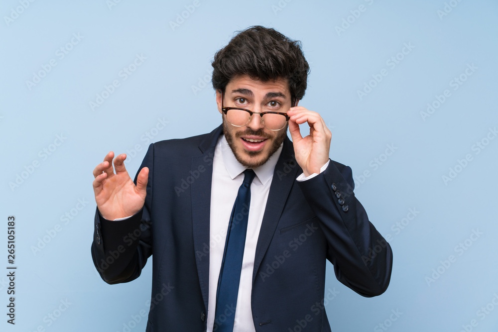 Businessman over isolated blue wall with glasses and surprised Businessman over isolated blue wall with glasses and surprised