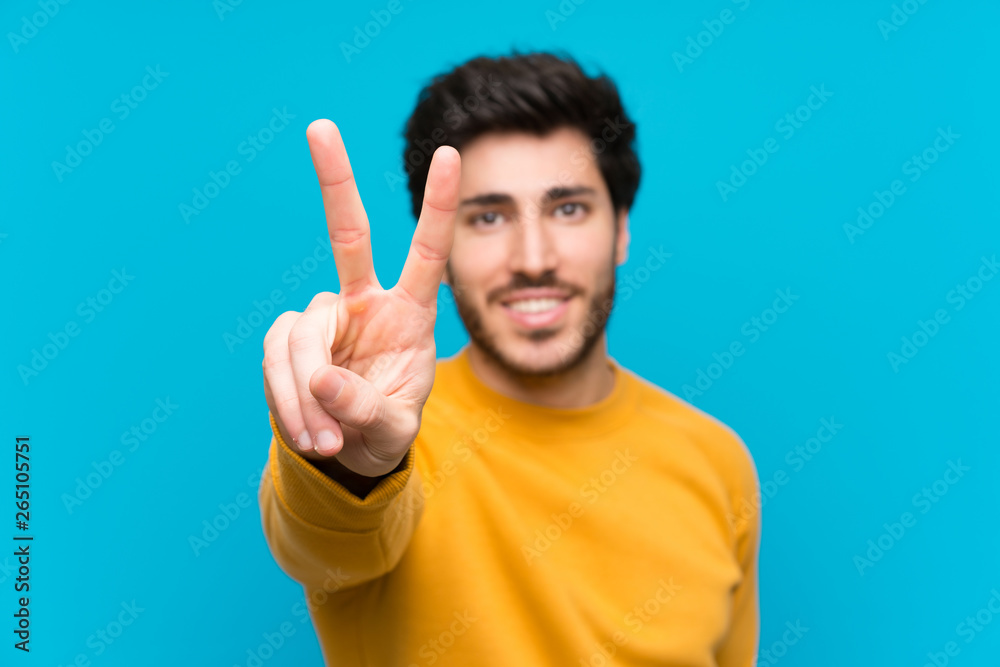 Handsome over isolated blue wall smiling and showing victory sign Handsome over isolated blue wall smiling and showing victory sign