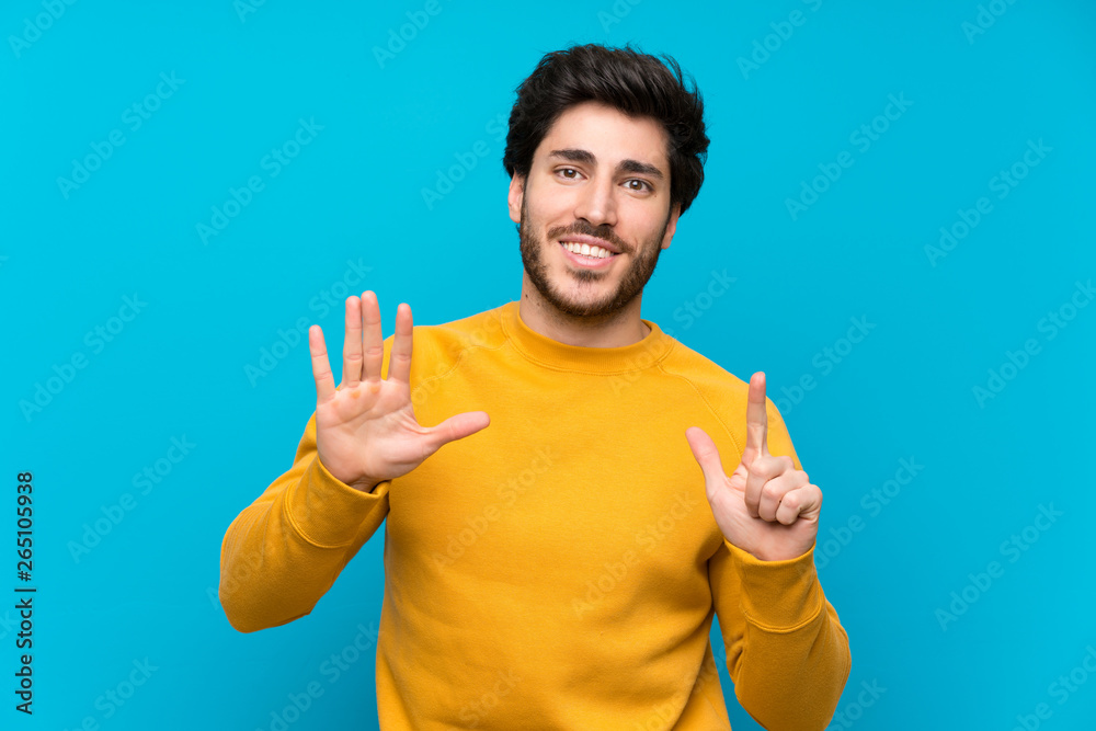 Handsome over isolated blue wall counting seven with fingers Handsome over isolated blue wall counting seven with fingers