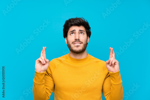 Handsome over isolated blue wall with fingers crossing and wishing the best