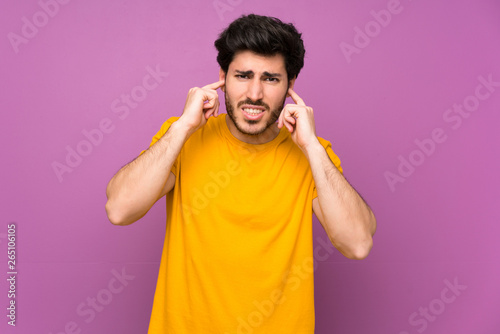 Handsome over isolated purple wall frustrated and covering ears