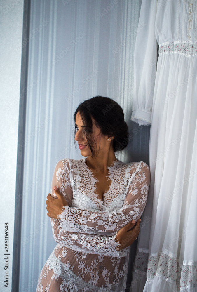 Fototapeta premium Beautiful cheerful happy woman in nightie is standing near a wedding dress. Laugh.