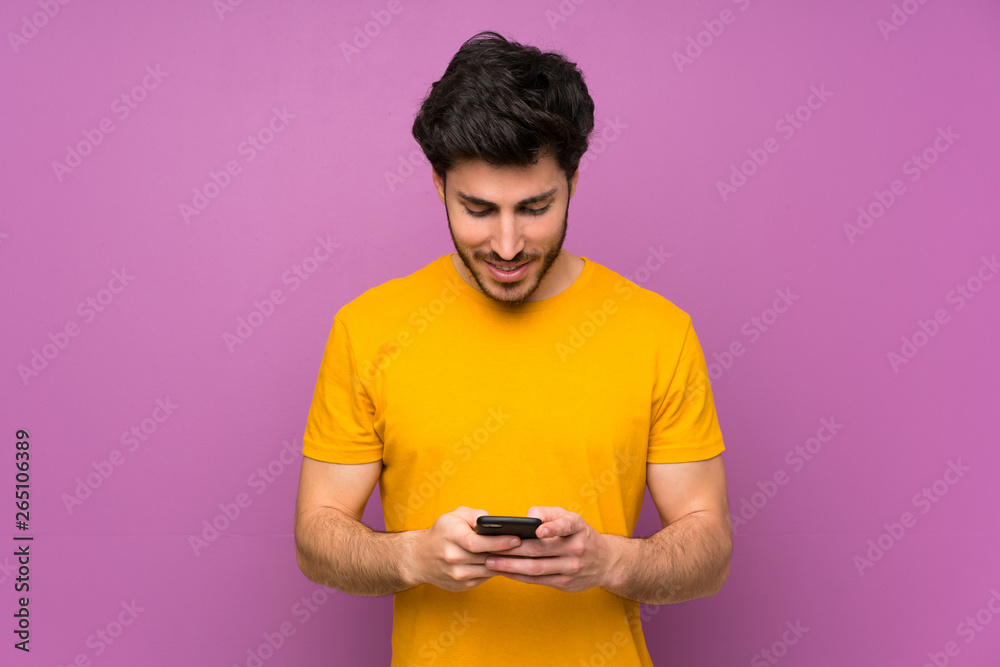 Handsome over isolated purple wall sending a message with the mobile Handsome over isolated purple wall sending a message with the mobile