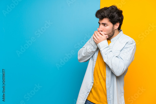 Handsome over isolated colorful background covering mouth and looking to the side