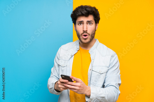 Handsome over isolated colorful background surprised and sending a message