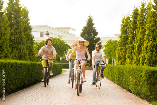 Happy friends riding bicycles on road in park. Four young cyclists outdoors. Summer tour by bikes. © DenisProduction.com