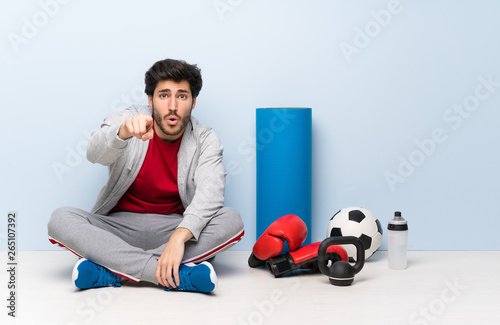 Sport man sitting on the floor surprised and pointing front