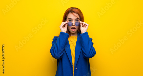 Young redhead woman with trench coat with glasses and surprised