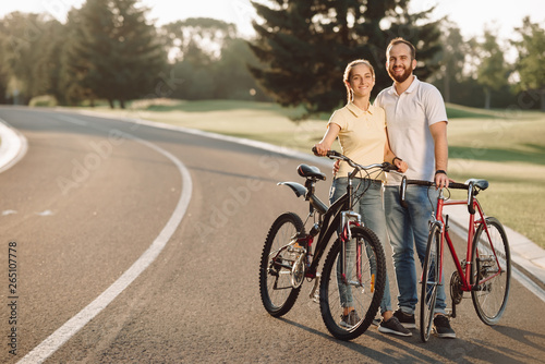 Couple of cyclists is smiling and looking at camera. Happy couple with bicycles outdoors. Romantic date with bikes.