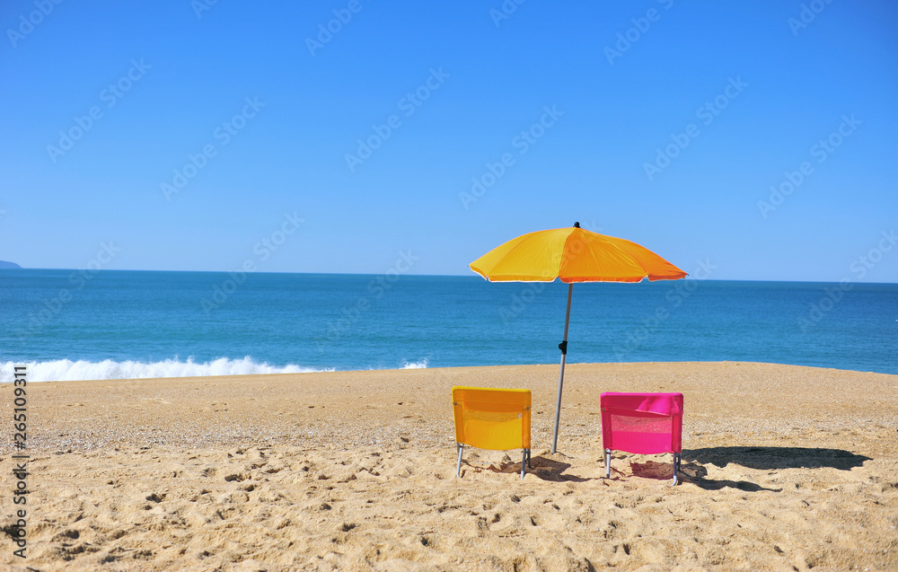 Two colorful beach chairs and umbrella with blue sea water