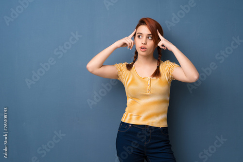 Young redhead woman over blue background having doubts and thinking © luismolinero