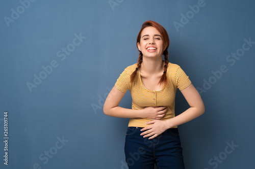 Young redhead woman over blue background smiling a lot while putting hands on chest