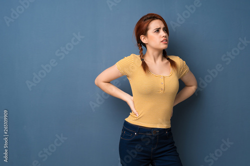 Young redhead woman over blue background suffering from backache for having made an effort