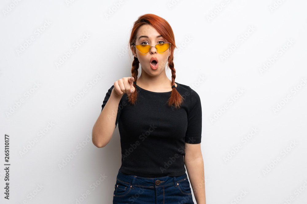 Young redhead woman over white wall surprised and pointing front Young redhead woman over white wall surprised and pointing front
