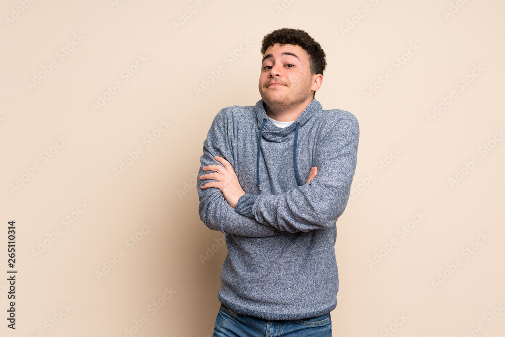 Young man over isolated wall making doubts gesture while lifting the shoulders Young man over isolated wall making doubts gesture while lifting the shoulders