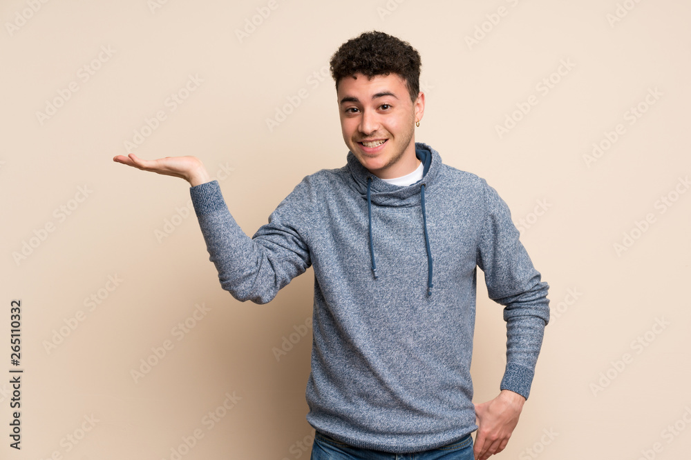 Young man over isolated wall holding copyspace imaginary on the palm to insert an ad