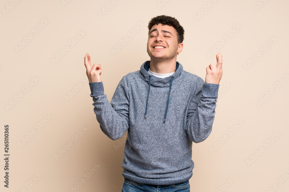 Naklejka premium Young man over isolated wall with fingers crossing and wishing the best
