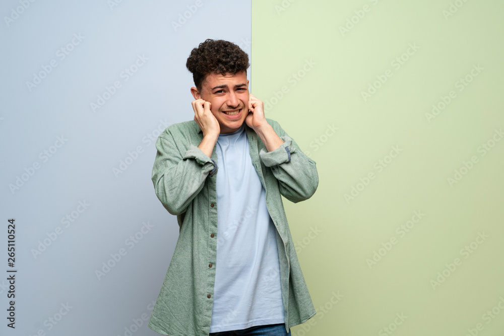 Young man over blue and green background covering ears with hands. Frustrated expression Young man over blue and green background covering ears with hands. Frustrated expression
