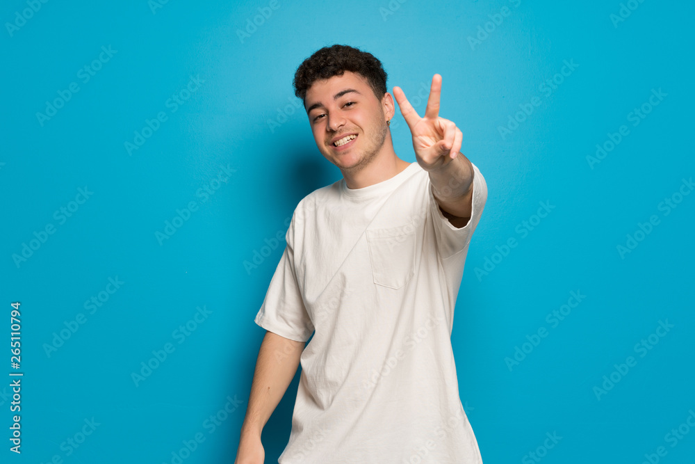 Young man over blue background smiling and showing victory sign