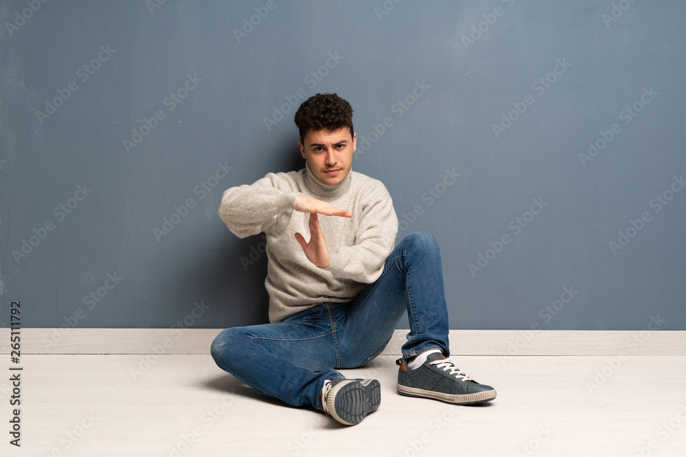 Young man sitting on the floor making time out gesture Young man sitting on the floor making time out gesture